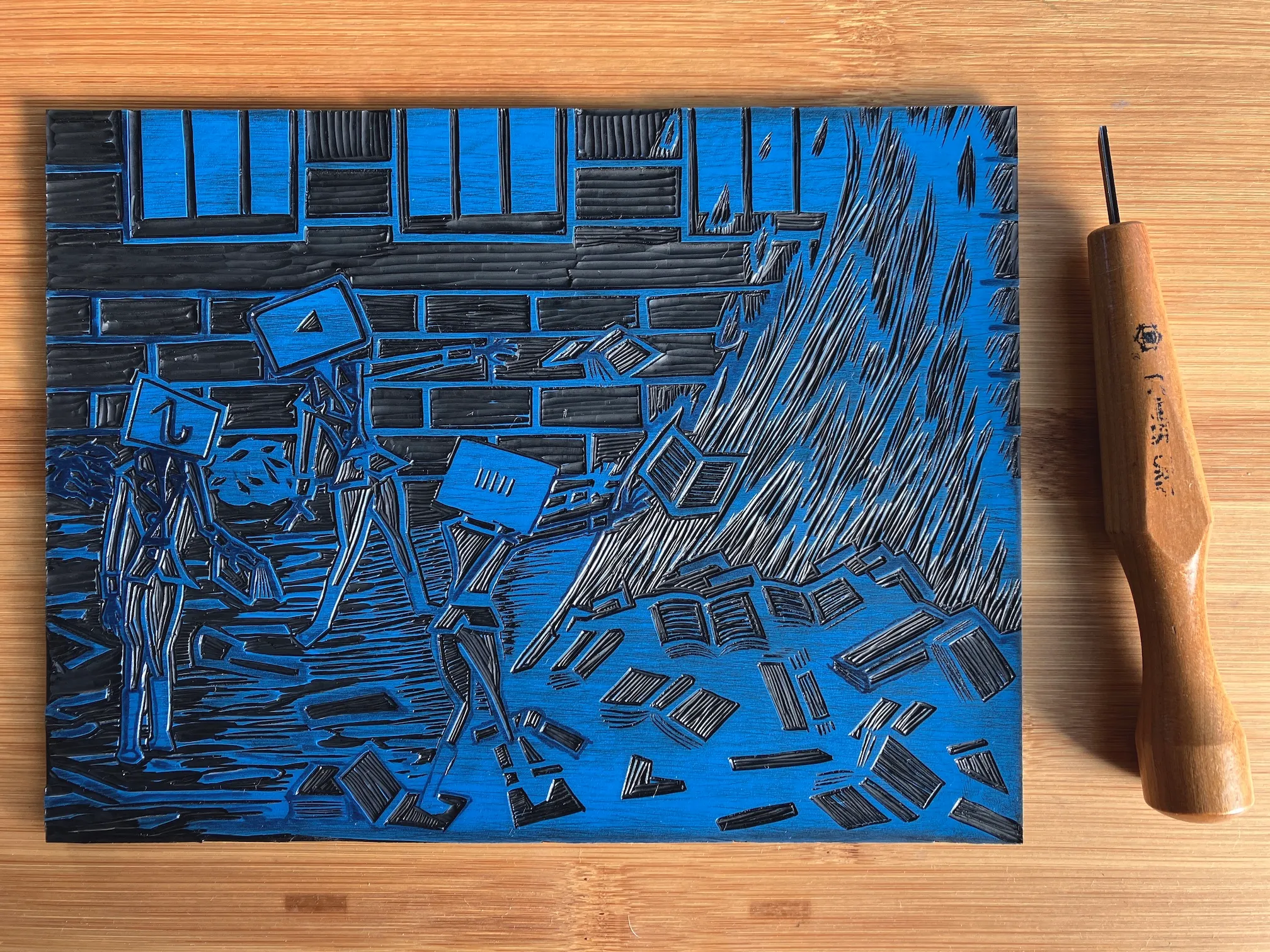 A vinyl plate into which the The End of Literacy print has been carved, alongside a small Japanese cutting tool.
