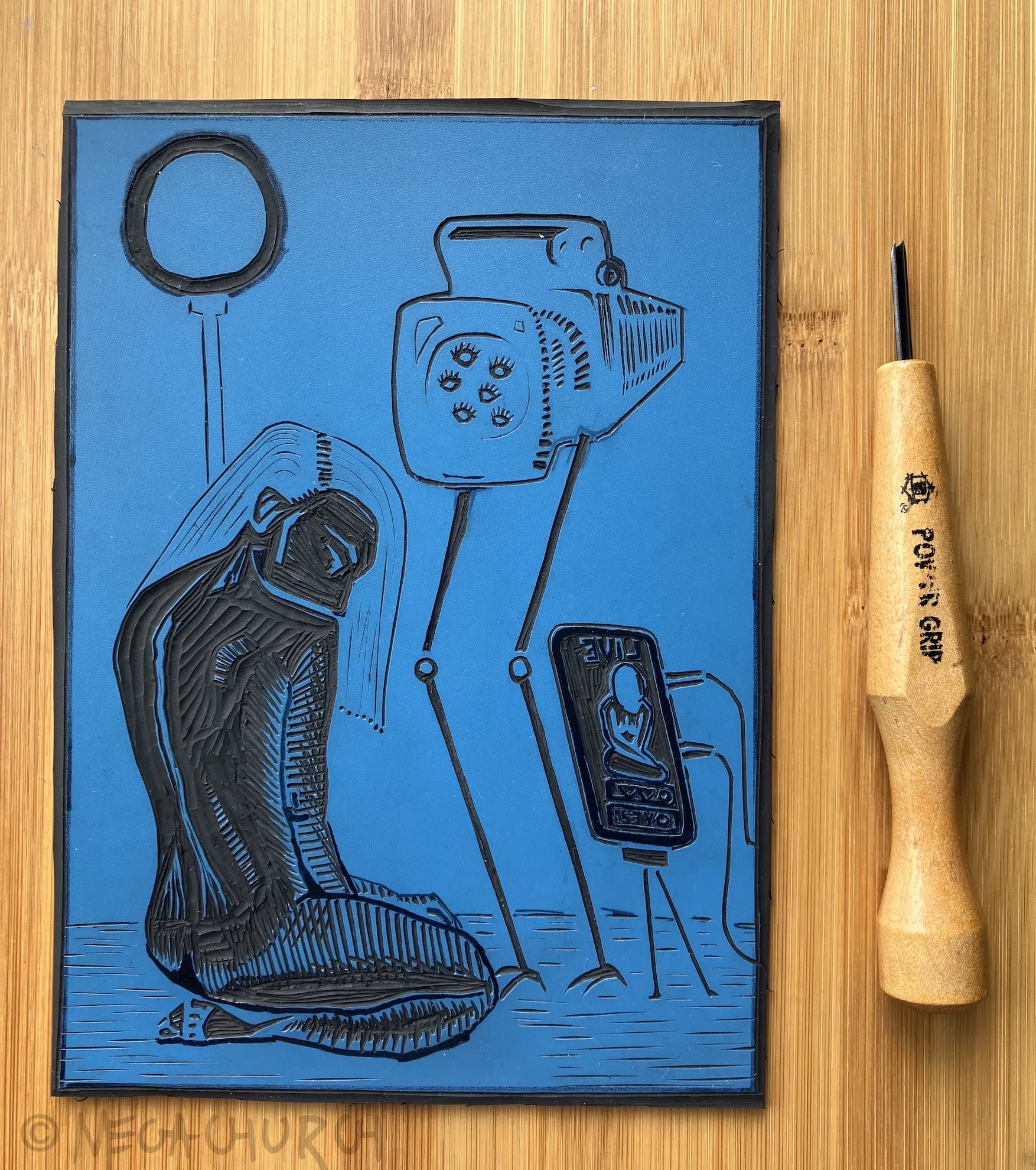 A vinyl plate into which the "Intimacy 2.0" print has been carved, alongside a small Japanese cutting tool.