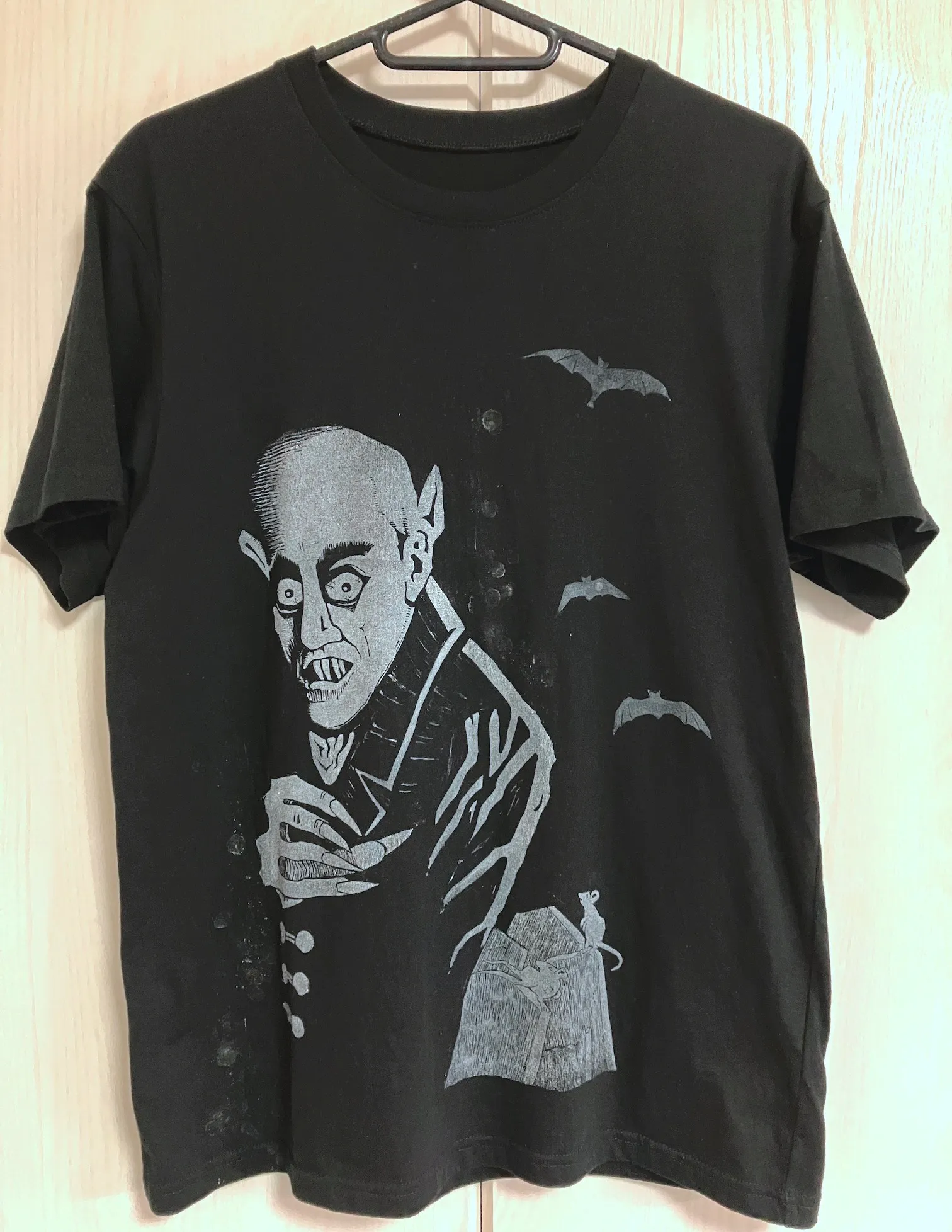 A black tee-shirt with the image of a menacing, goggly-eyed, pointy-eared vampire on it. The vampire stands in a graveyard. Bats rise in the background.