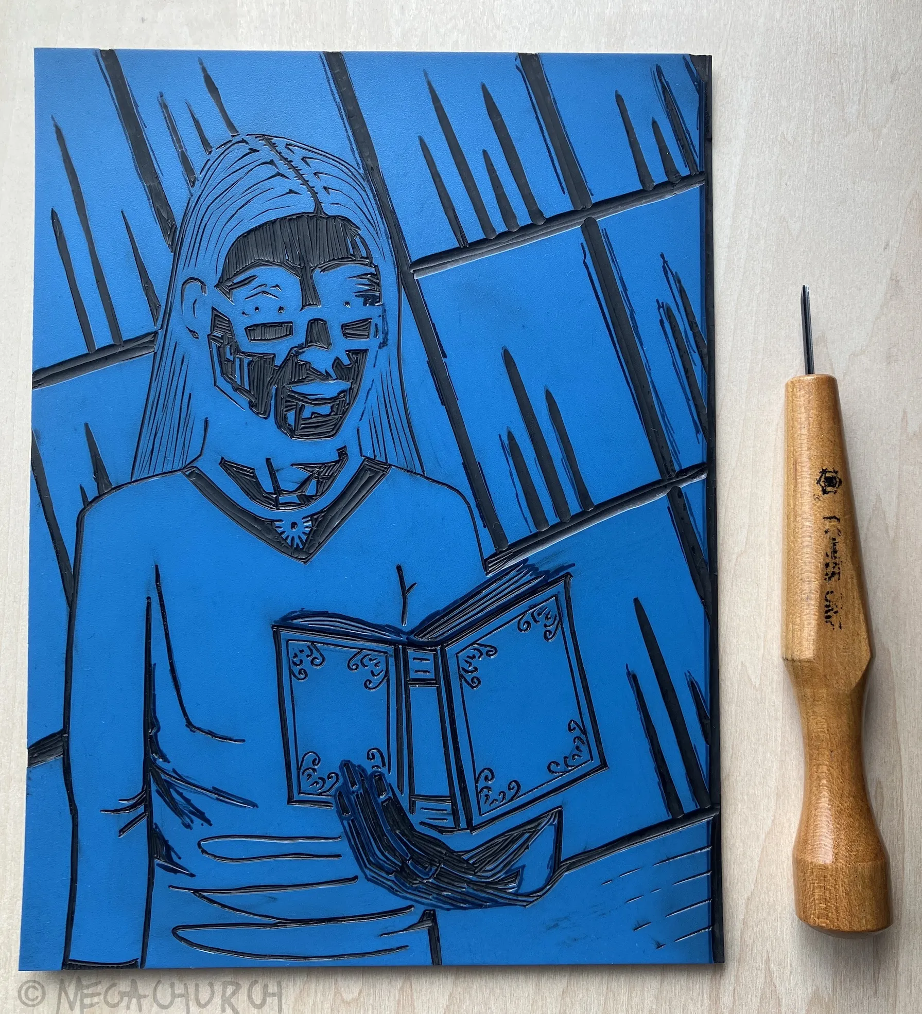 A vinyl plate into which the "Woman Reading" print has been carved, alongside a small Japanese cutting tool.