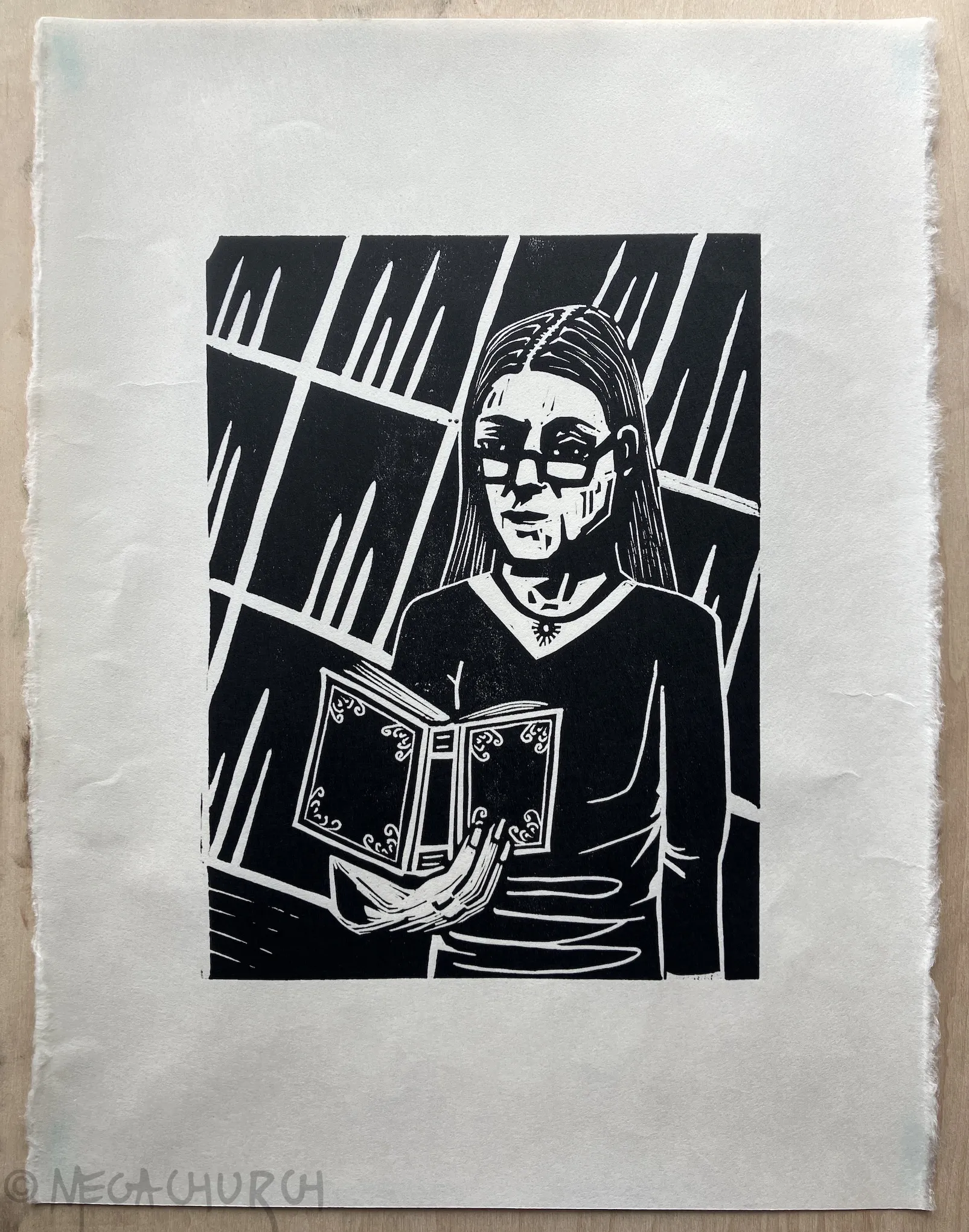 A relief print of a woman wearing glasses holding an open book in her hand with an ornate cover. She appears to be reading.